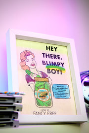 Framed artwork with a vintage-style illustration of a woman holding a jar labeled 'Blimpy Boy' on a shelf.