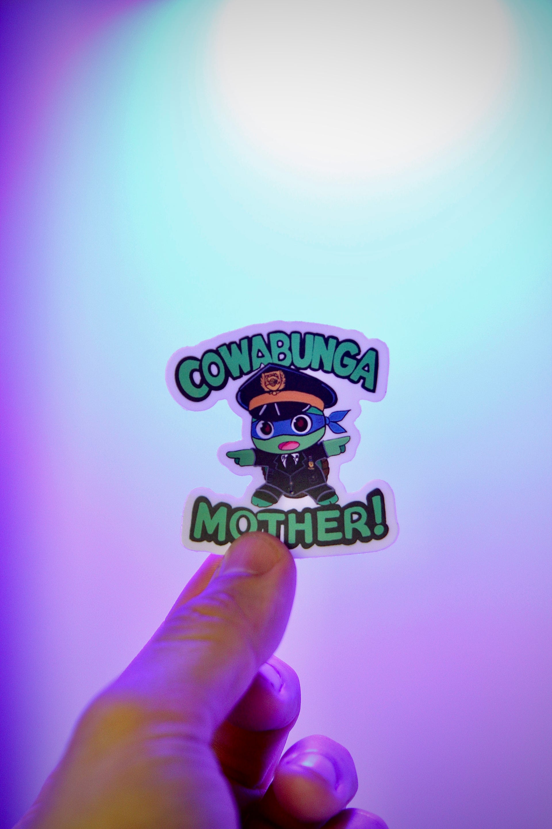 Sticker with cartoon character and text held by a hand against a colorful background