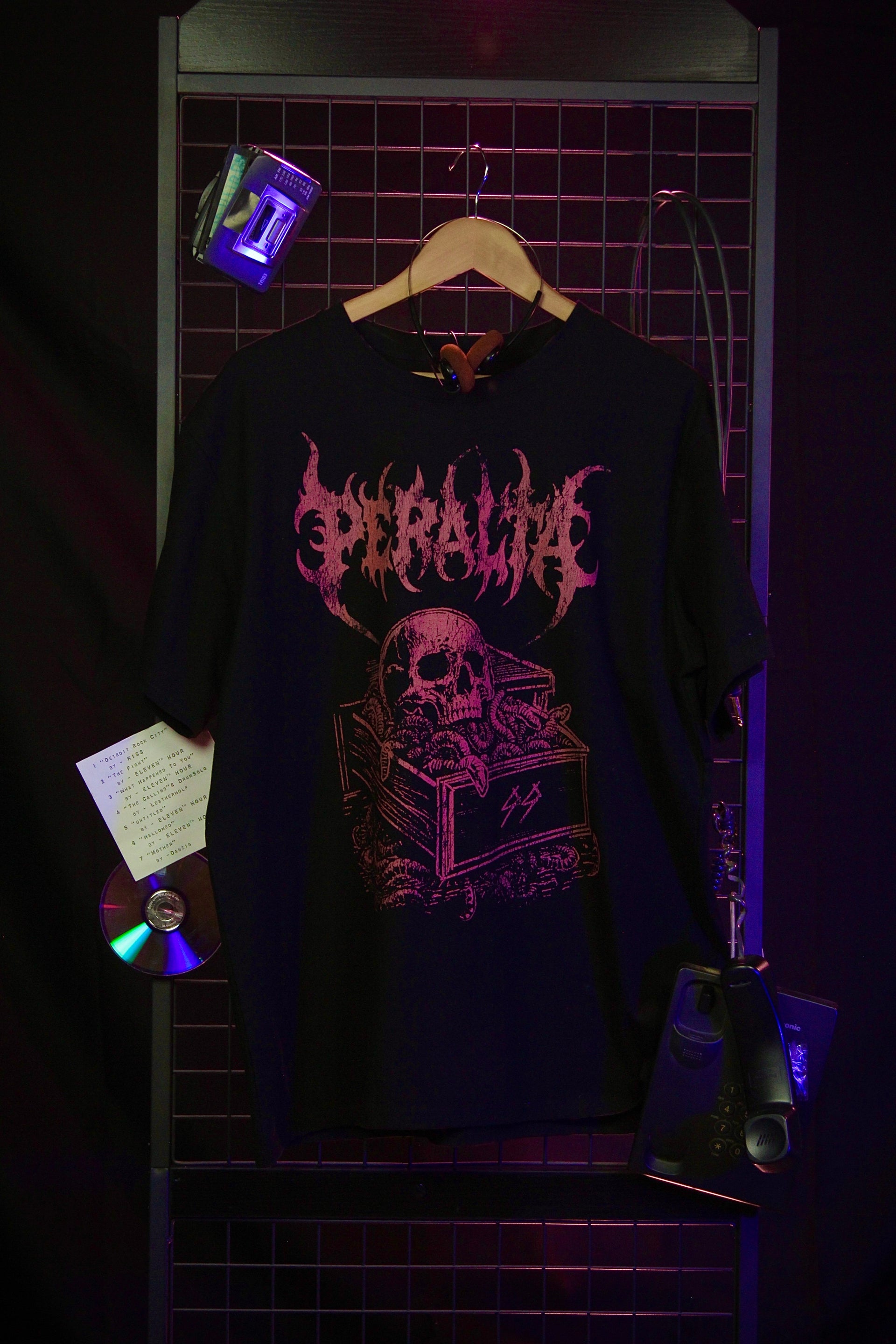 Black t-shirt with pink graphic design on a hanger against a dark background