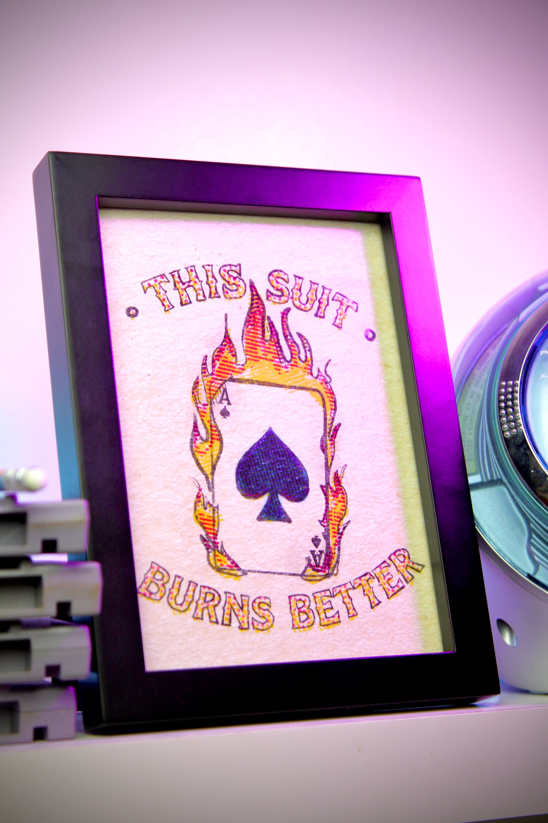 Framed artwork with a purple spade symbol and text 'This suit burns better' on a white background.